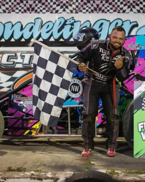 A driver in a custom suit holding a checkered flag at the track