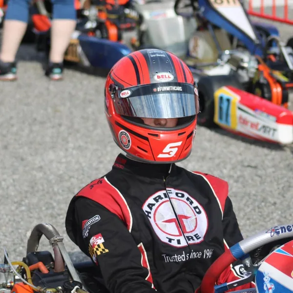 Young kart racer Ryan Denher in his custom black and red suit and red helmet, sitting in his kart